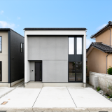 シンプルなグレーの外観に、軒と袖壁がつくる陰影が建物に奥行きをもたらし、街並みに自然と溶け込みながらも印象に残るデザインの住まい。